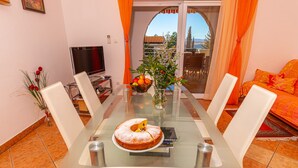 A dining area with a glass table, white chairs, a cake, and a fruit bowl. - Apartment Dadi (Crikvenica)