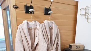 Two beige bathrobes hanging on a wooden wall-mounted rack in a room with a fireplace and a radiator. - B&B 43 4 (Le Puy-en-Velay)