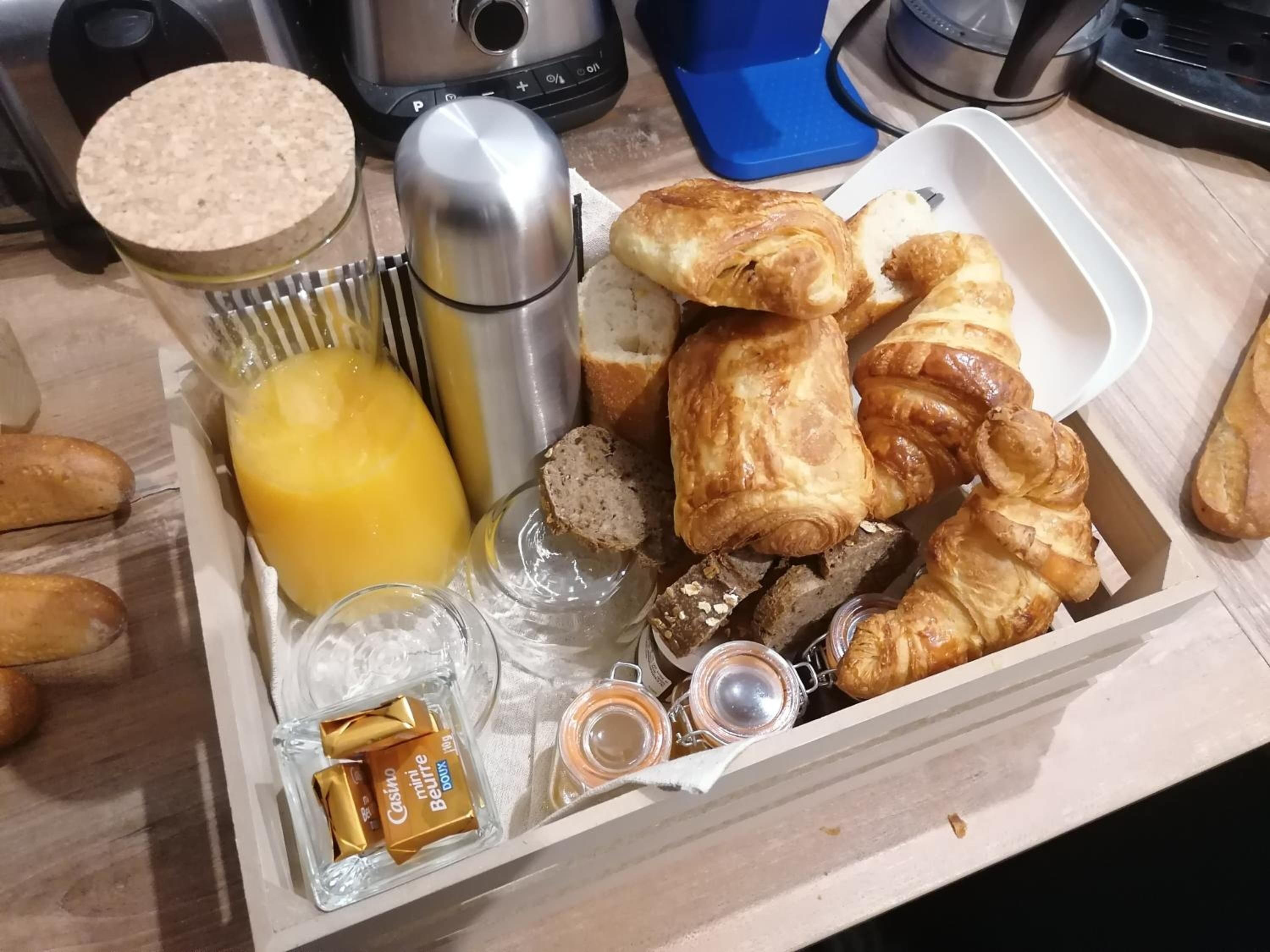 A tray with croissants, a thermos, a glass of juice, and a jar of jam.