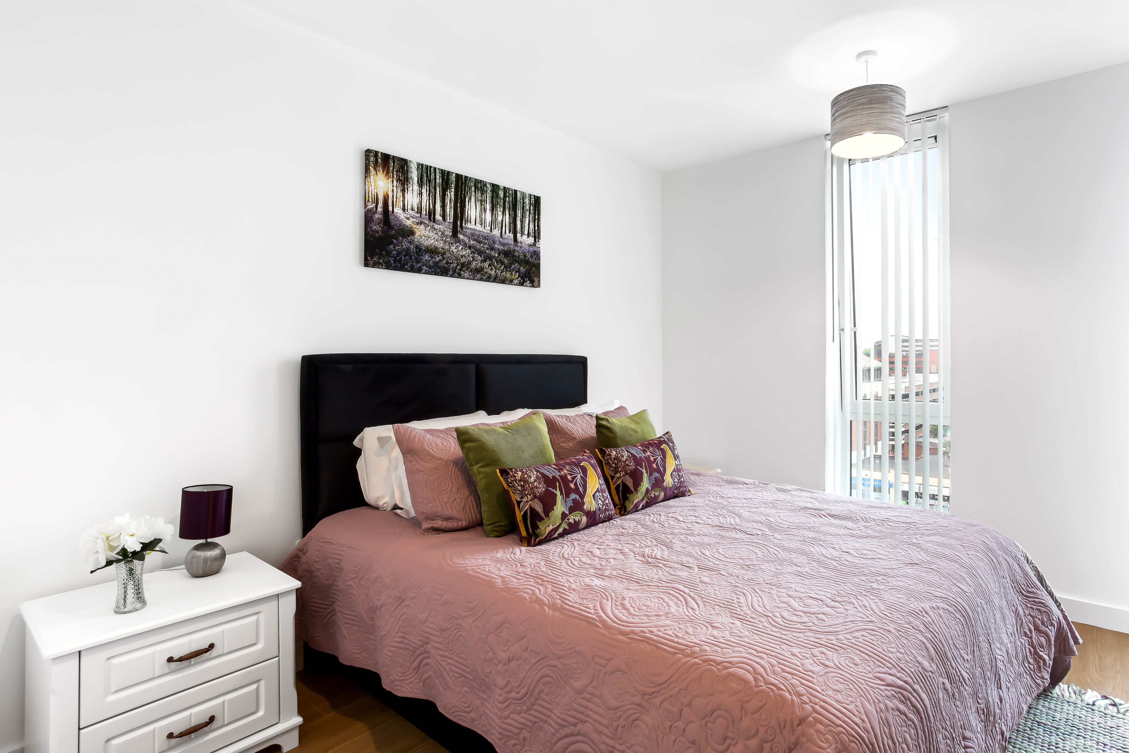 A bedroom with a bed, a nightstand, a lamp, and a painting on the wall.