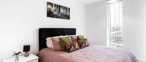 A bedroom with a bed, a nightstand, a lamp, and a painting on the wall.