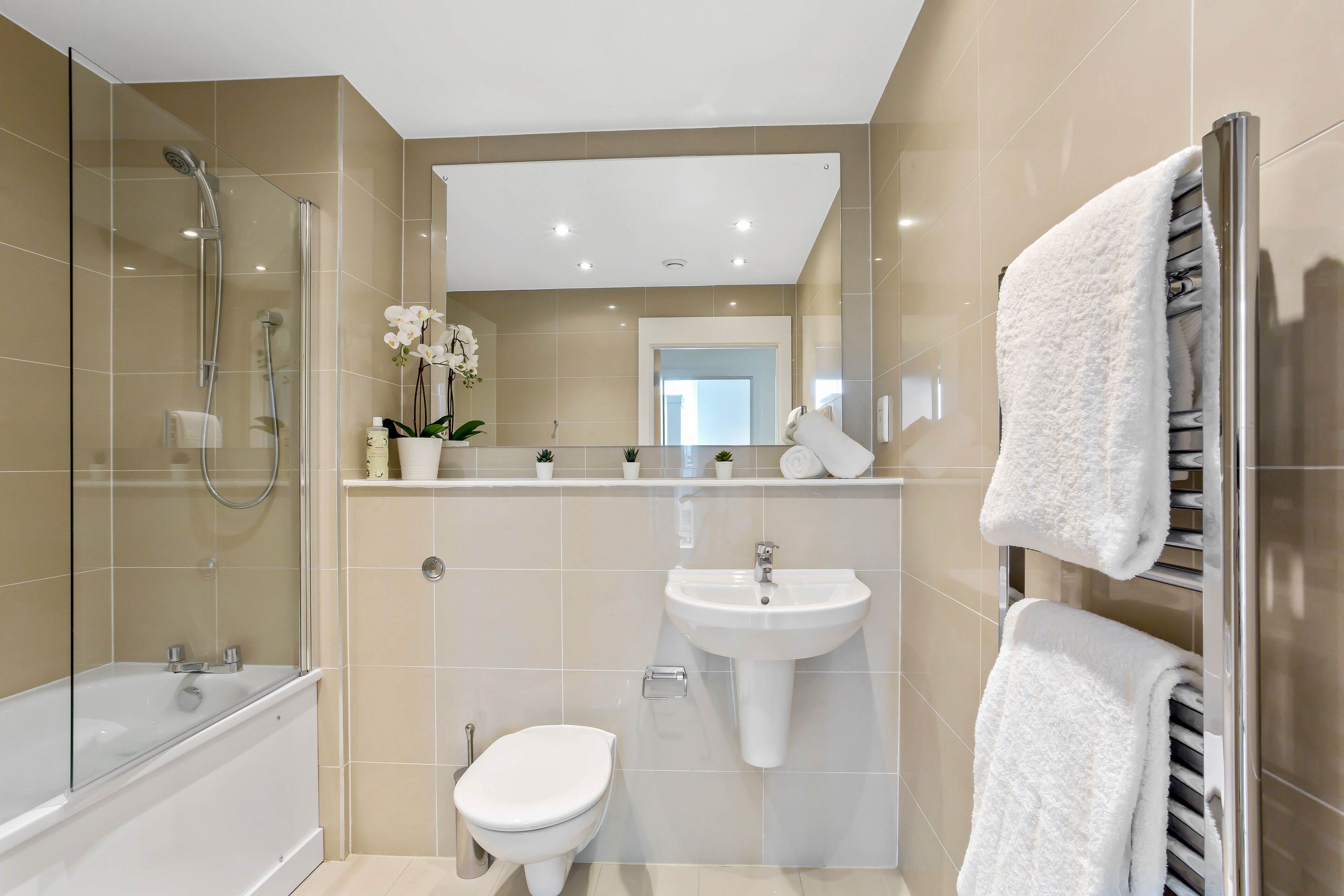 A modern bathroom with a glass-enclosed shower, a white bathtub, a sink, and a toilet.