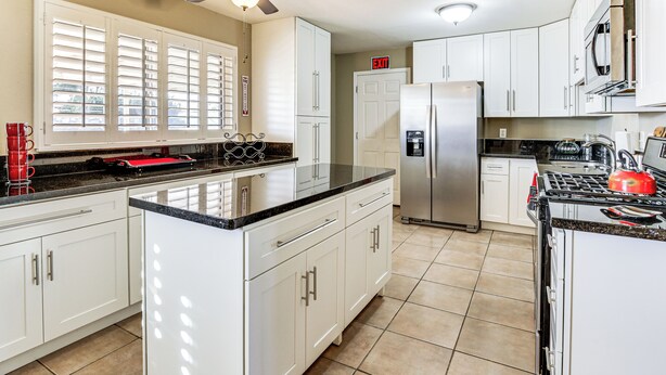Una cocina moderna con armarios blancos, un refrigerador de acero inoxidable, una estufa a gas y un ventilador de techo.