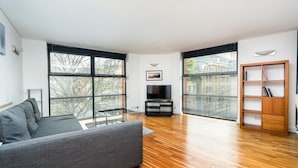 A modern living room with a grey sofa, a TV stand, and a wooden bookshelf. - Broadband 2BD City Flat Farringdon Expedia (London)