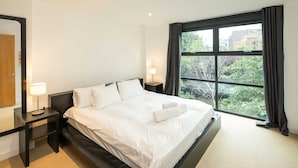 A modern hotel room with a large bed, two bedside tables, a nightstand, and a large window with curtains. - Broadband 2BD City Flat Farringdon Expedia (London)