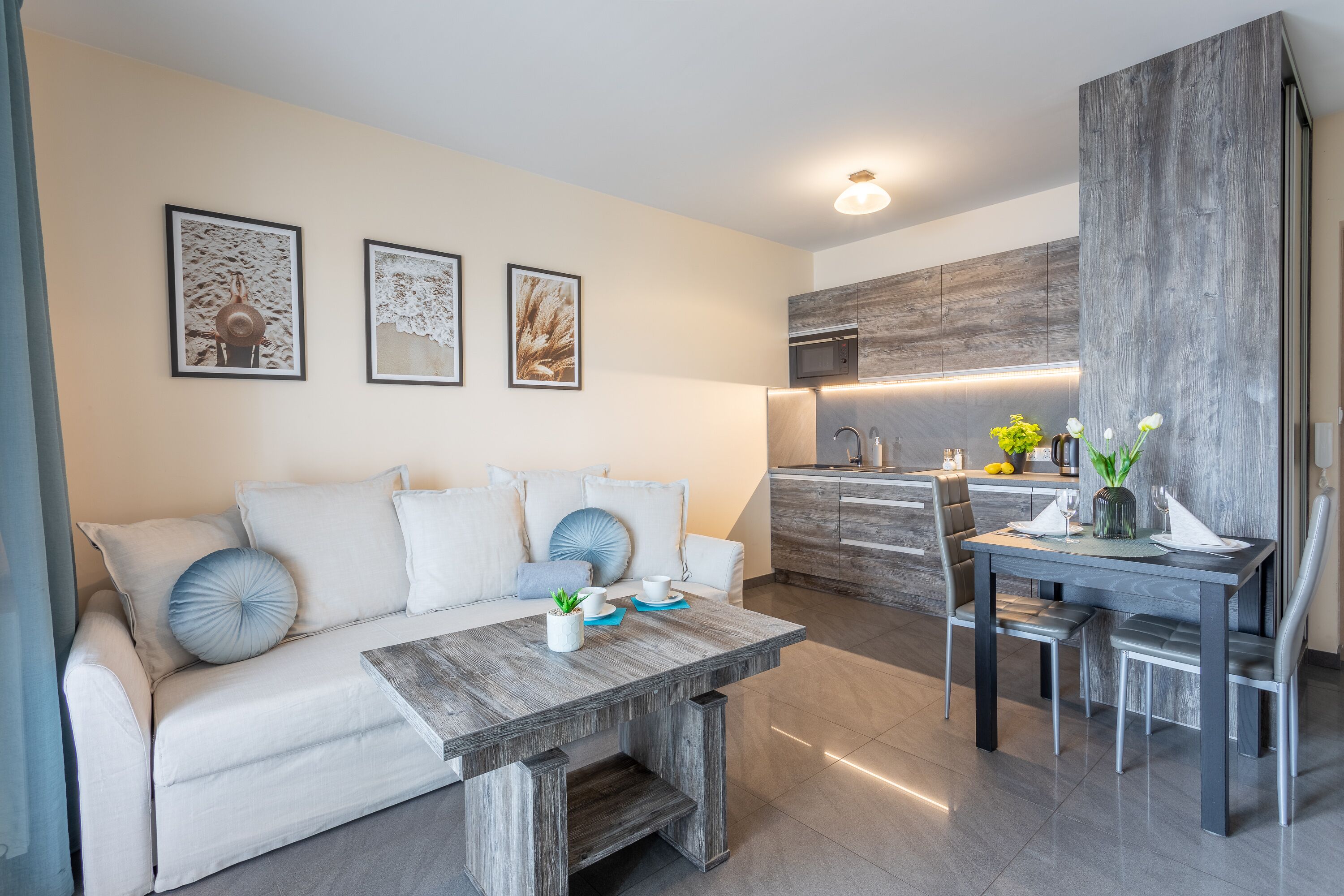 A modern living room with a sofa, coffee table, and dining area with chairs. There is a kitchen in the background with a wooden accent wall.