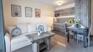 A modern living room with a sofa, coffee table, and dining area with chairs. There is a kitchen in the background with a wooden accent wall. - Vacation apartment by the sea, vacation on the island of Usedom, Apartment AURORA (Świnoujście)