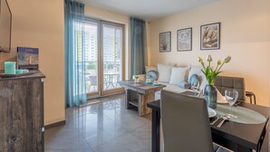 A modern living room with a sofa, coffee table, and dining area. There are framed pictures on the wall, a window with curtains, and a view of the outside. - Vacation apartment by the sea, vacation on the island of Usedom, Apartment AURORA (Świnoujście)