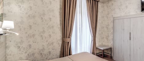 A hotel room with a bed, a small table, a lamp, and a wardrobe.