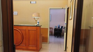 Un hall d’hôtel avec un comptoir d’accueil, une chaise, une lampe et une porte portant l’inscription « MILO ».