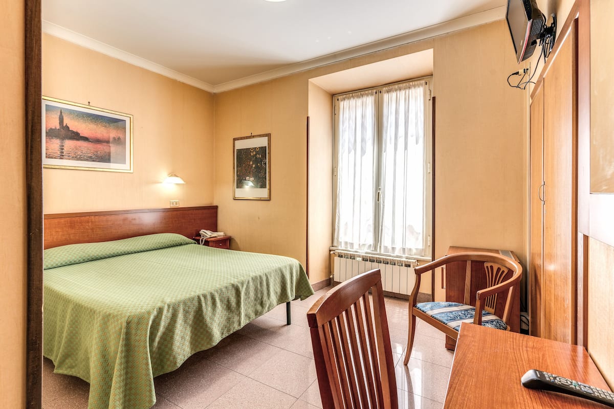 A hotel room with a bed, a chair, a table, a lamp, and a window with curtains.