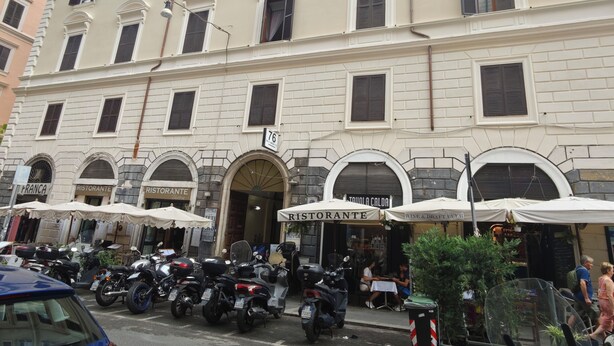 Un immeuble à plusieurs étages, orné d’enseignes de restaurants, avec des motos garées et des espaces de restauration en plein air.
