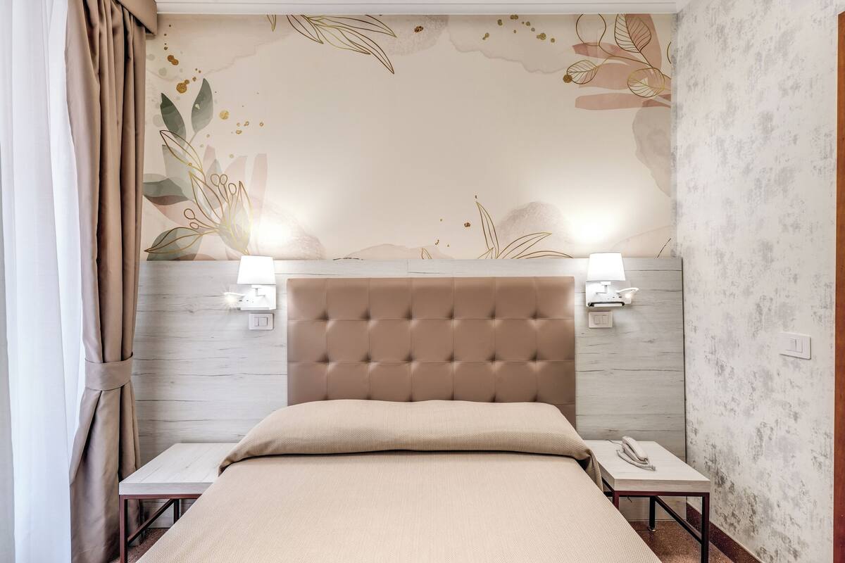 A bedroom with a tufted headboard, two bedside tables with lamps, and a floral wall mural.
