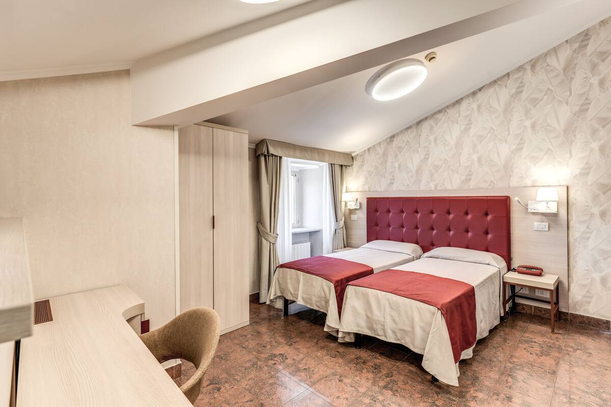 A hotel room with two beds, a desk, a chair, and a window with curtains.
