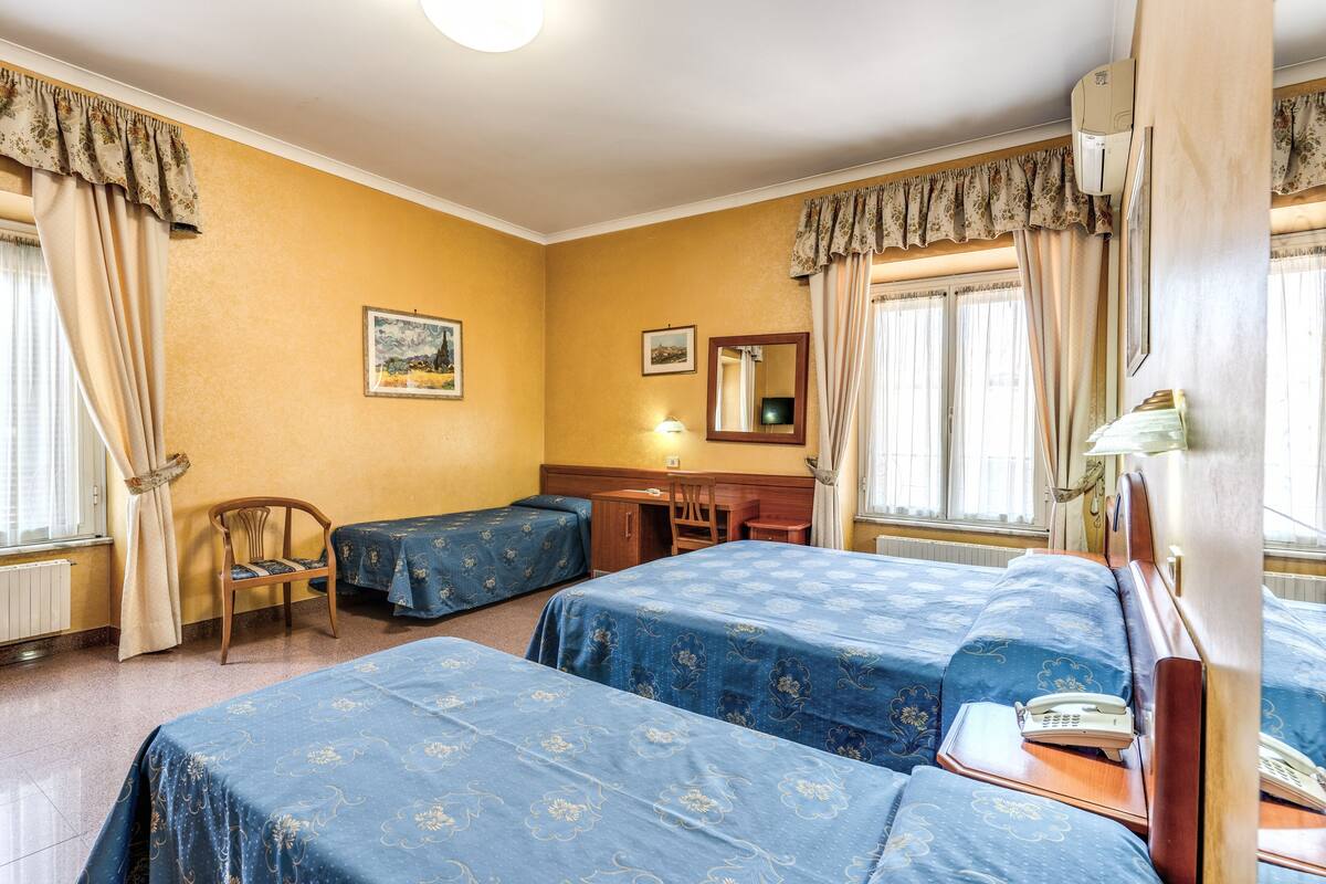 A hotel room with two beds, a desk, a chair, a telephone, and a window with curtains.
