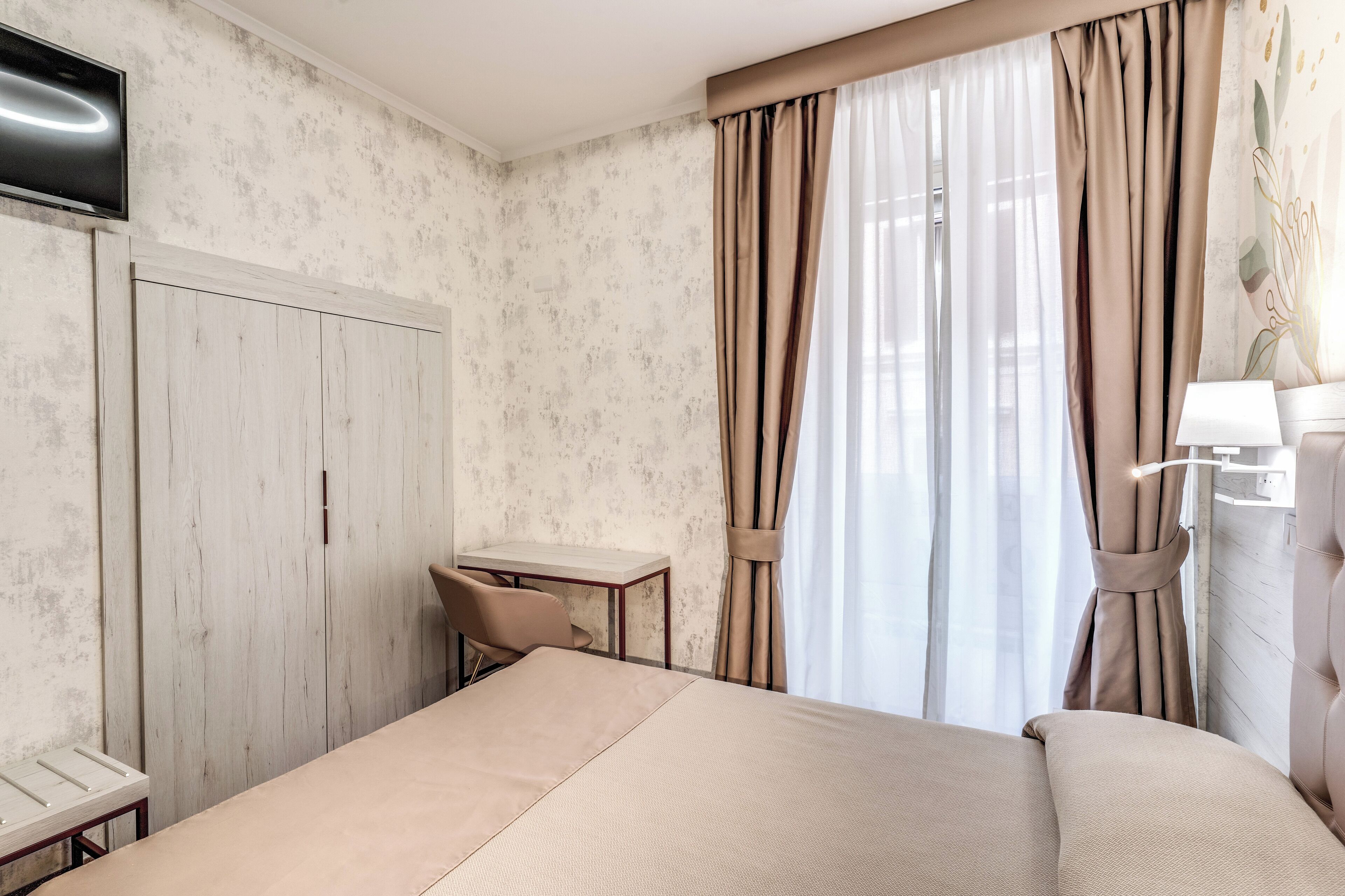 A hotel room with a bed, a desk, a chair, and a TV.