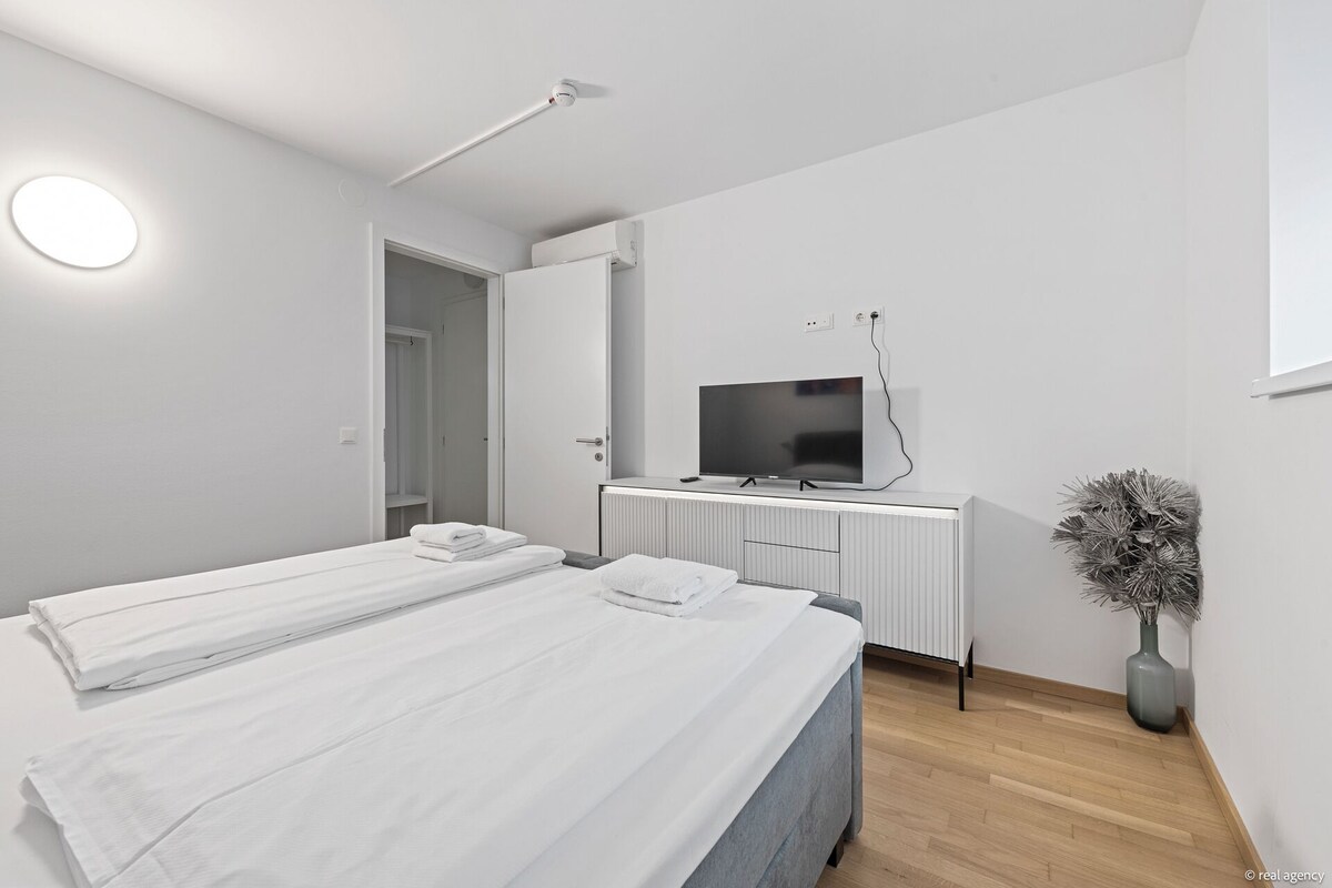 A modern bedroom with a bed, a desk with a TV, a radiator, and a potted plant.