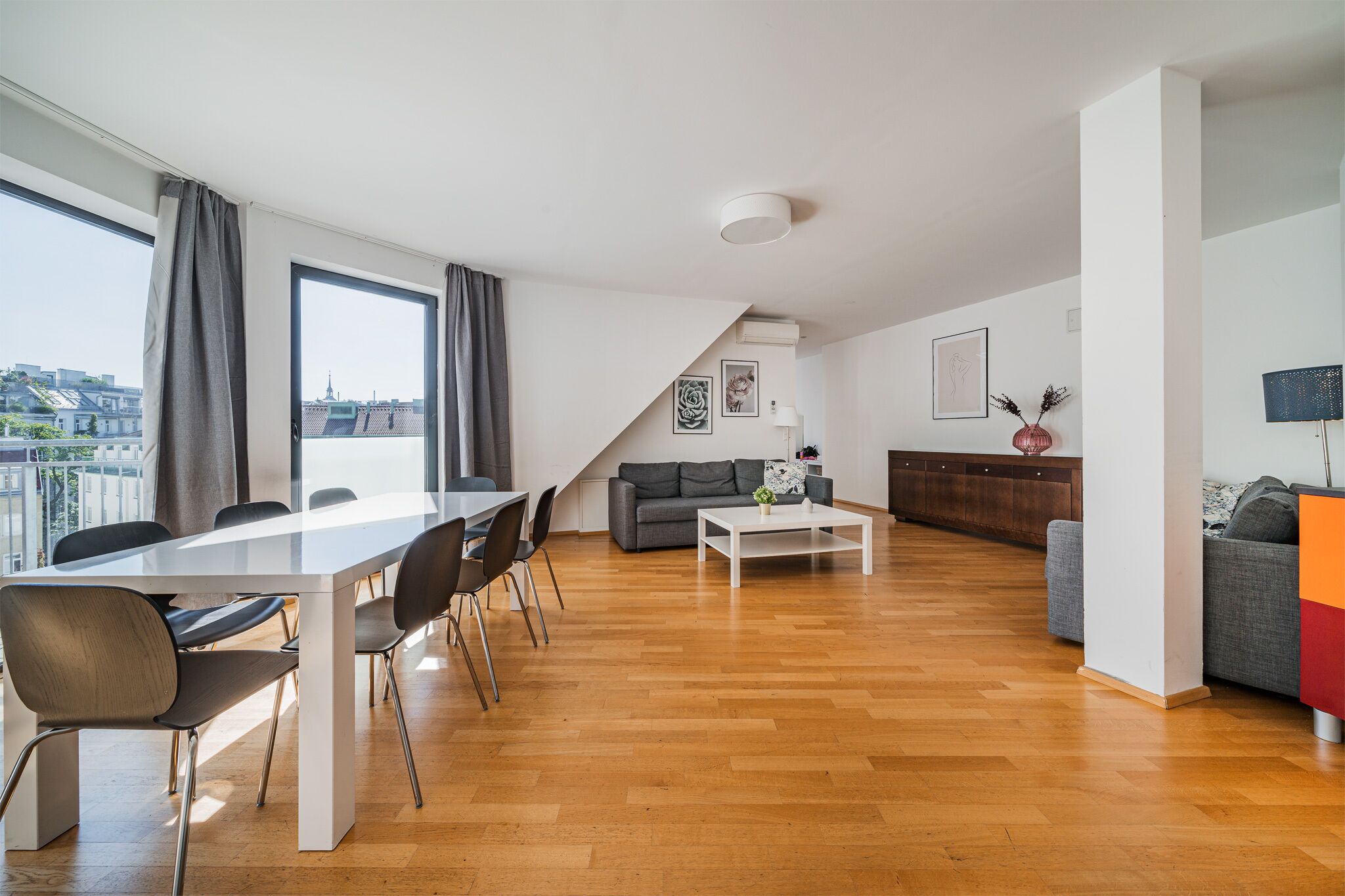 A modern apartment with a dining area, sofa, and a view of the city.