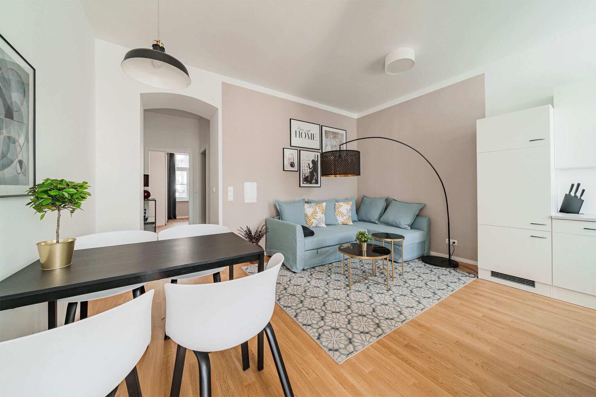 Una sala de estar moderna con sofá, una mesa de centro y zona de comedor. Hay una cocina con armarios y un refrigerador.