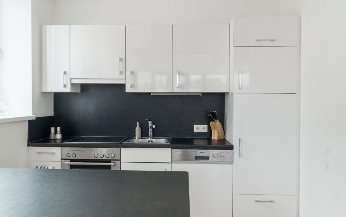 A modern kitchen with white cabinets, a black countertop, stainless steel appliances, and a knife block.
