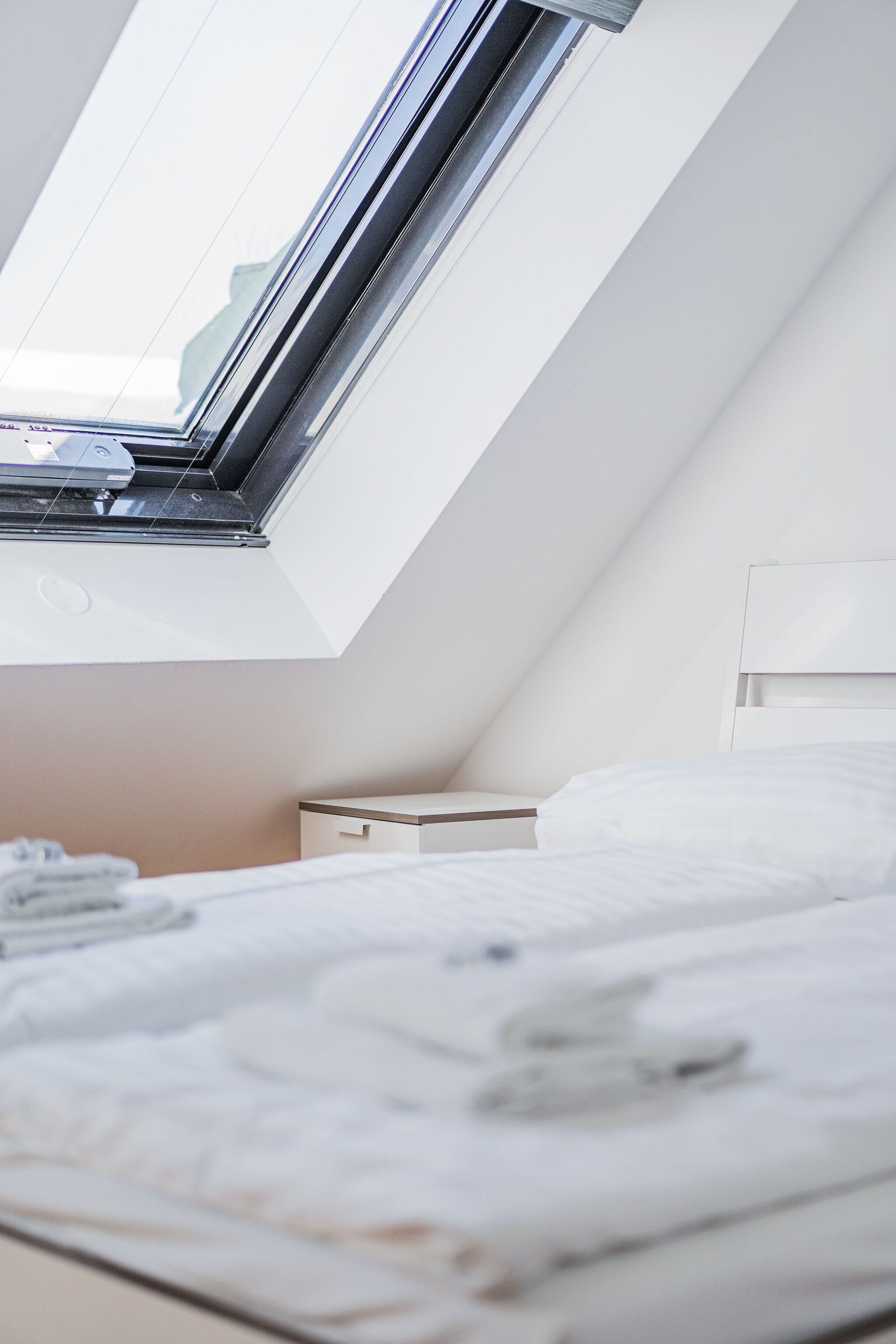 A bedroom with a skylight, a bed, a bedside table, and a nightstand.
