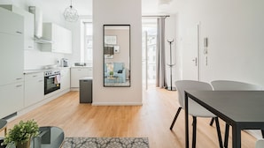Una cocina moderna con armarios blancos, horno empotrado y comedor con mesa y sillas.