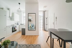 A modern kitchen with white cabinets, a built-in oven, and a dining area with a table and chairs. - easy-flat Pilgramgasse - Apartments near Metro (Vienna)