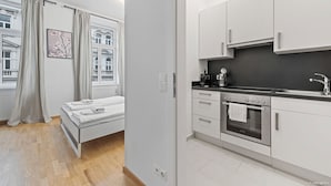 Habitación de hotel moderna con cama, kitchenette y vista a un edificio a través del ventanal.