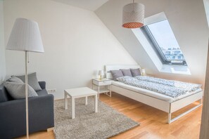 A modern bedroom with a sloped ceiling, a bed with a patterned bedspread, a grey sofa, a small white table, a floor lamp, and a view through a skylight. - easy-flat Pilgramgasse - Apartments near Metro (Vienna)