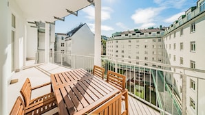 Un balcón con una mesa y sillas de madera, con vistas a un paisaje urbano que incluye edificios y un área verde.