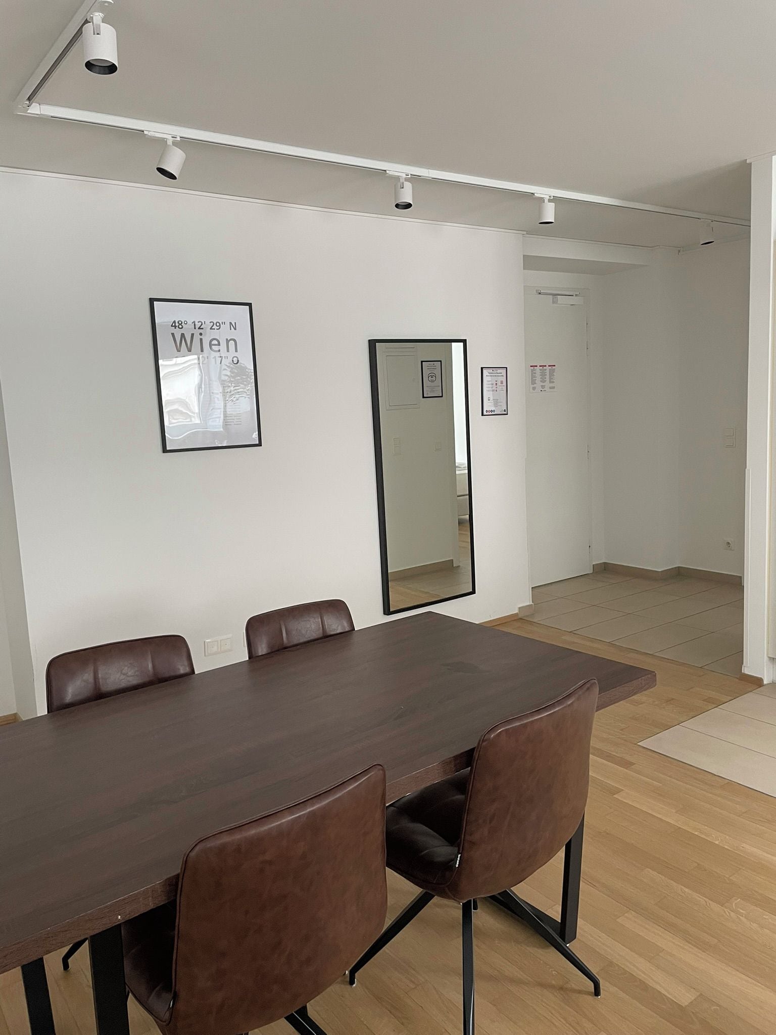 A conference room with a long table, six chairs, and a large mirror on the wall.