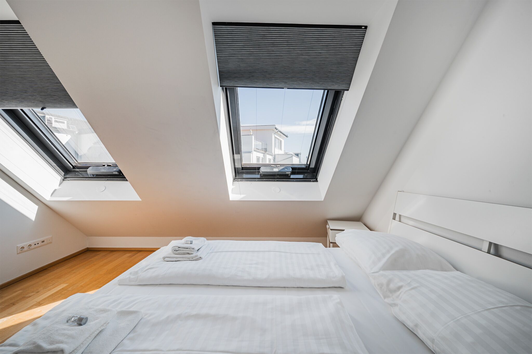A modern bedroom with a skylight, a neatly made bed, and a view of buildings through the window.
