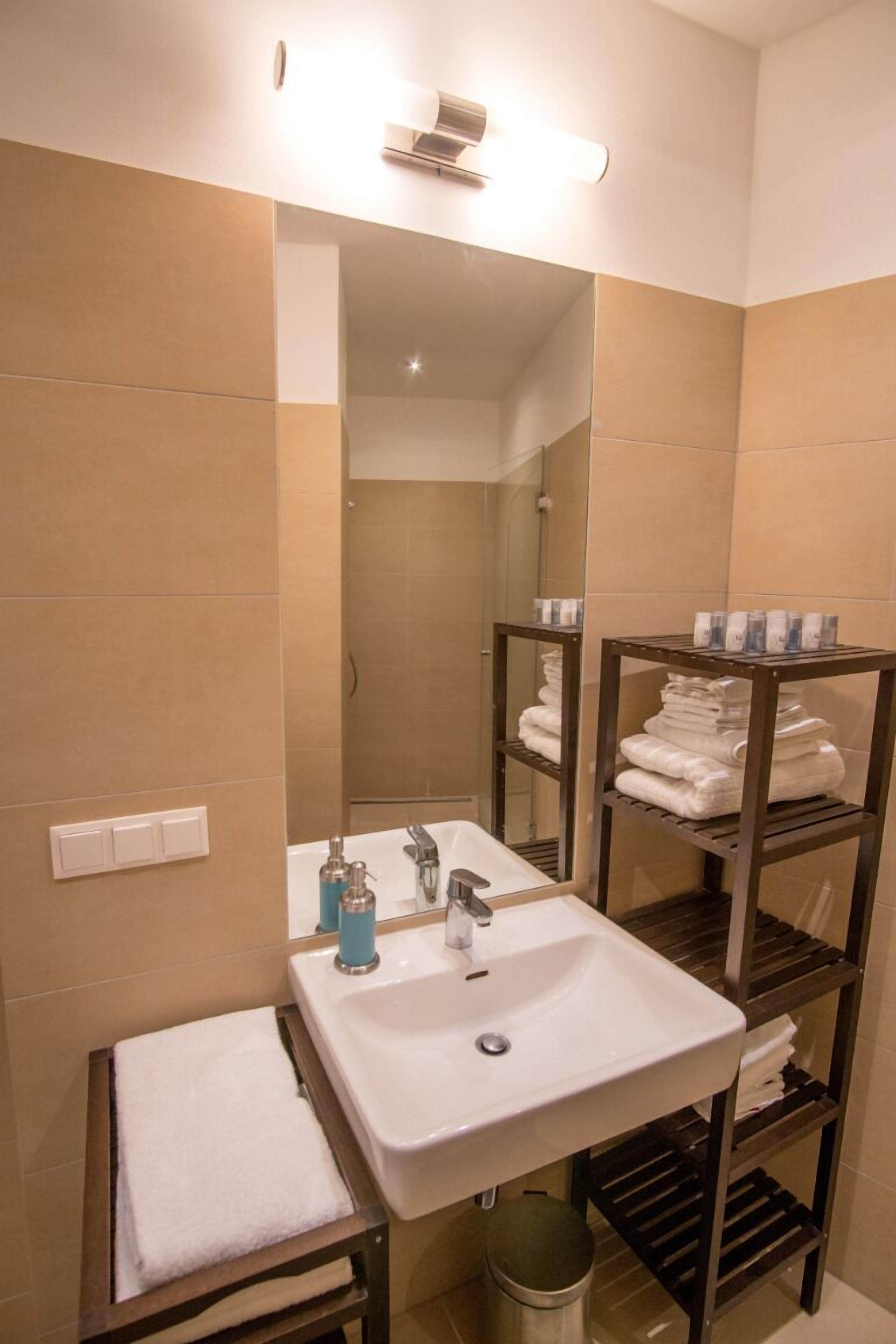 Un baño con lavamanos blanco, espejo y repisas con toallas.