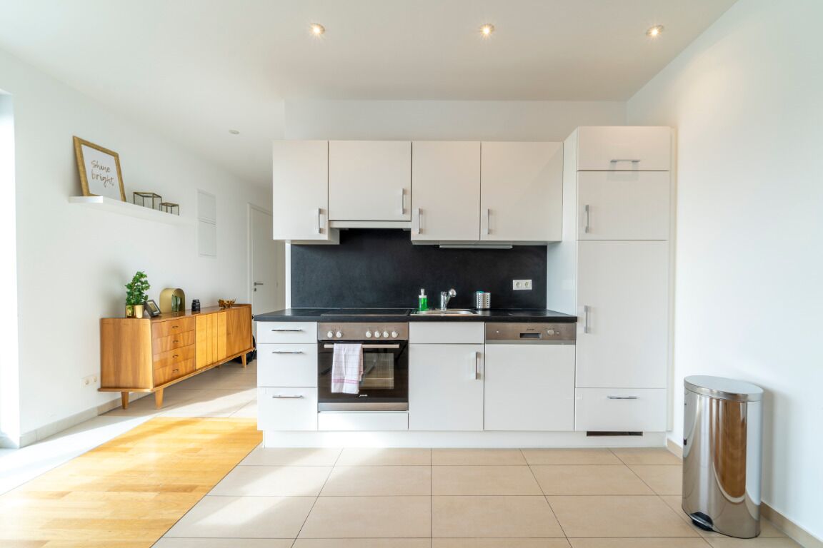 A modern kitchen with white cabinets, a black countertop, and a wooden cabinet on the left.