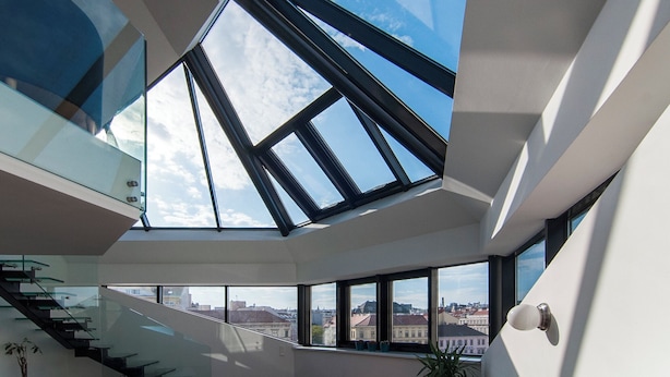 Un interior moderno con una escalera de cristal, ventanas amplias y vistas a la ciudad.