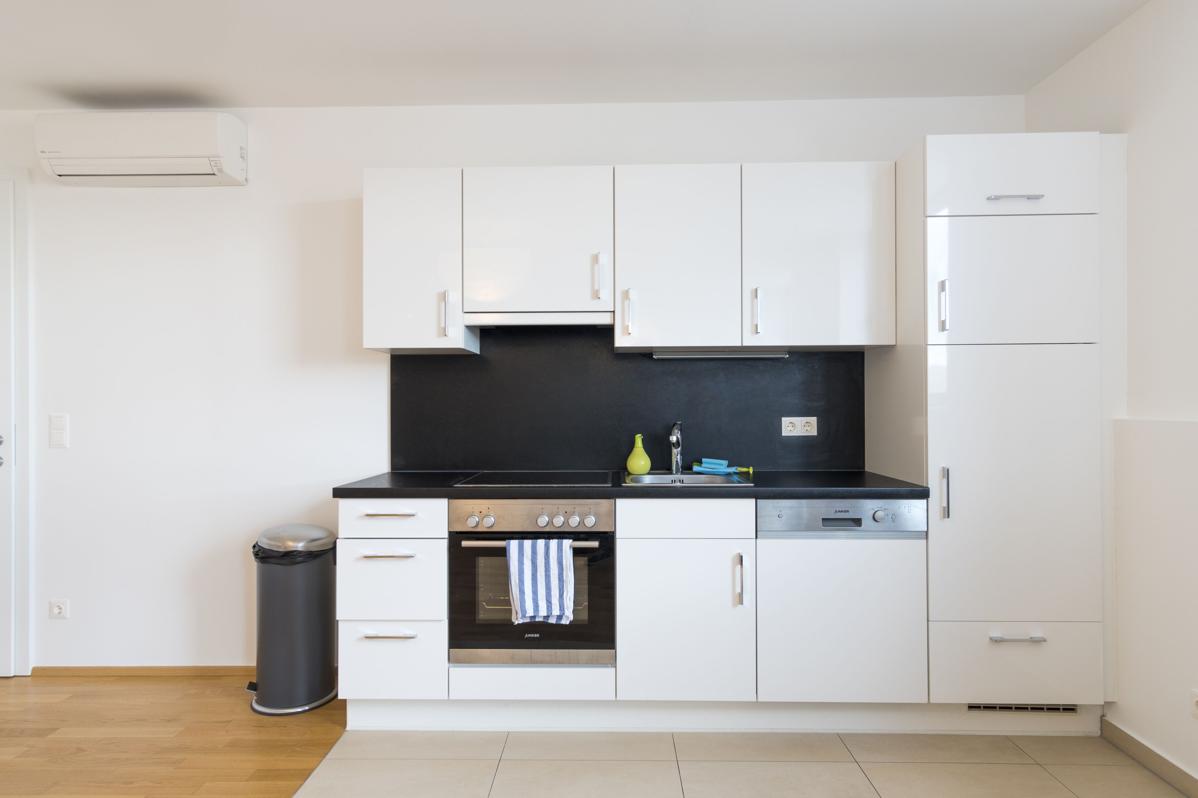 A modern kitchen with white cabinets, a black countertop, stainless steel appliances, and a trash bin.