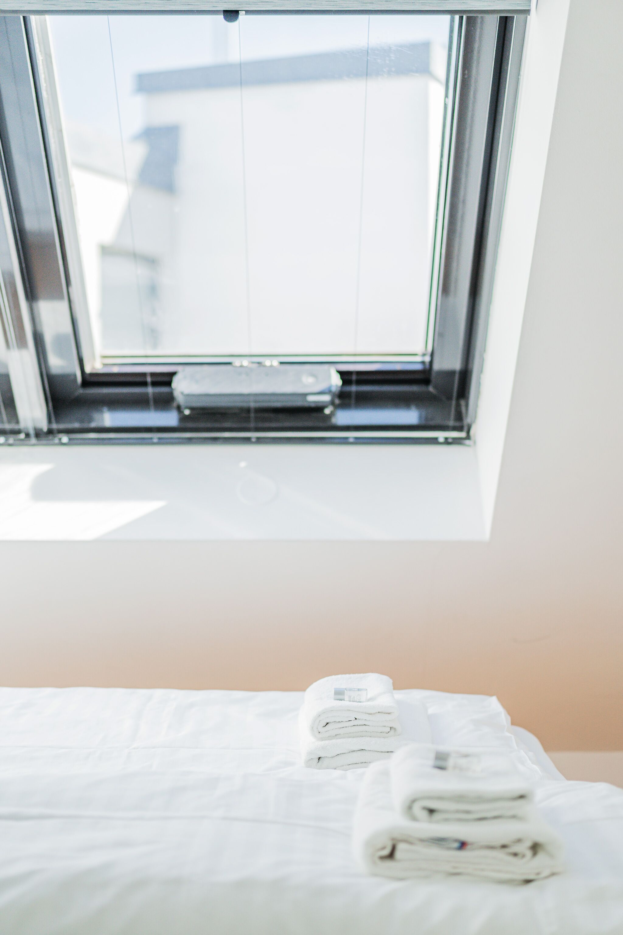 Ett hotellrum med ett takfönster, en säng med prydligt vikta vita handdukar och utsikt över himlen.