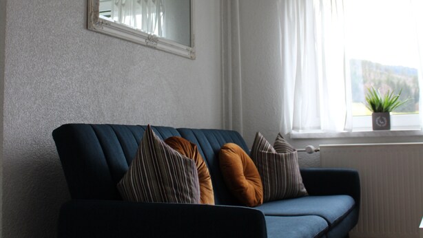 Una sala de estar moderna con un sofá azul oscuro, un espejo en la pared y una ventana con cortinas blancas.