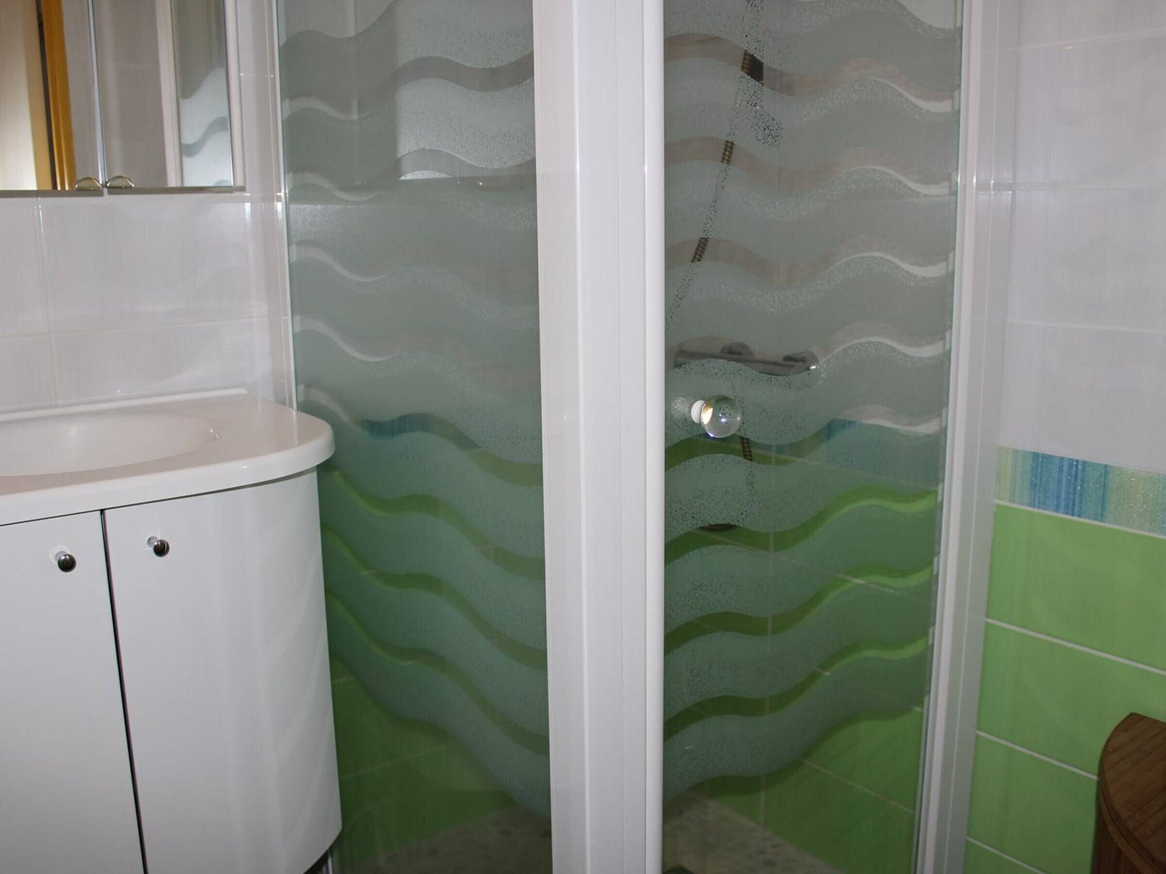 A bathroom with a white sink, frosted glass shower enclosure, and green tiled walls.