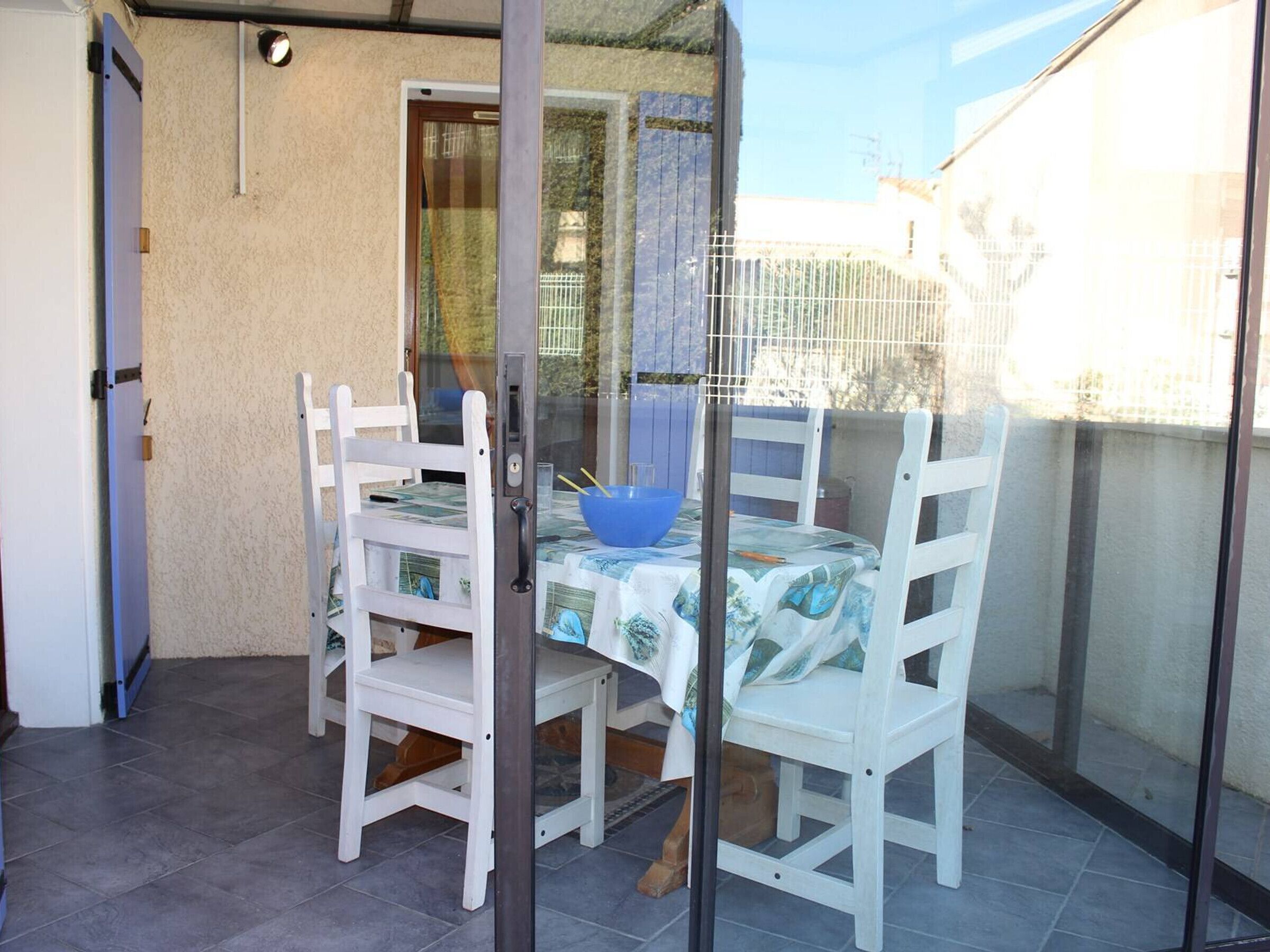 Een klein terras met een tafel, stoelen, een blauwe kom en een deur naar een overdekt gedeelte.