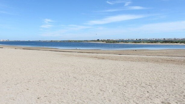 Een breed zandstrand met een rustige zee en een heldere lucht.