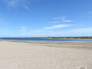 En bred, sandet strand med et roligt hav og en klar himmel.