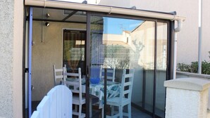Een glazen patio met een tafel en stoelen, een schuifpui en uitzicht op een woonwijk.