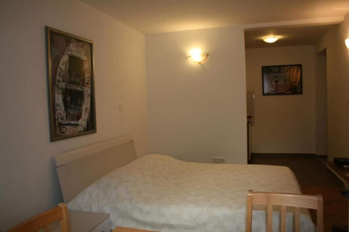 A bedroom with a bed, a chair, a painting on the wall, and a light fixture.