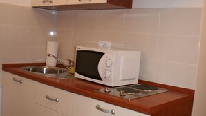 Keittiössä on valkoiset kaapit, ruostumattomasta teräksestä valmistettu pesuallas ja mikroaaltouuni.