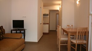 Kompakti olohuone, jossa on sohva, televisio, ruokapöytä tuoleineen ja taustalla keittiö.
