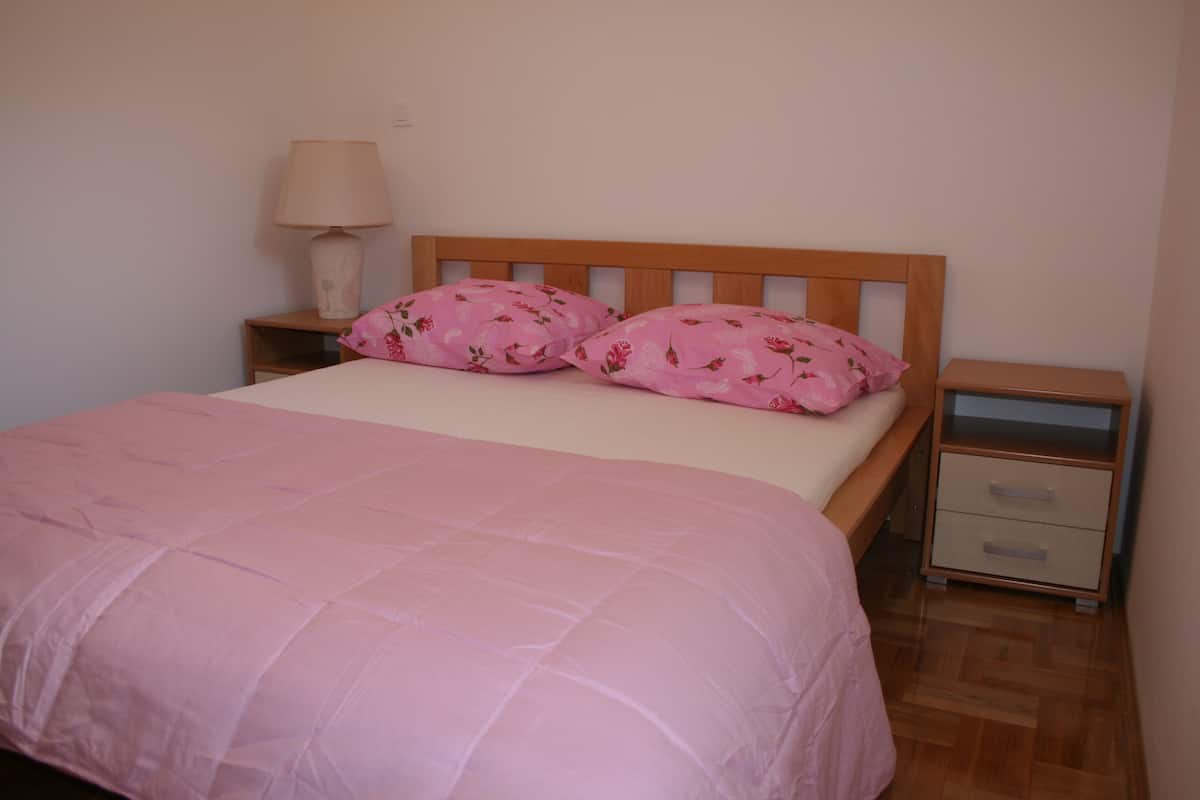 A bedroom with a wooden bed, pink bedding, a bedside lamp, and a nightstand with drawers.