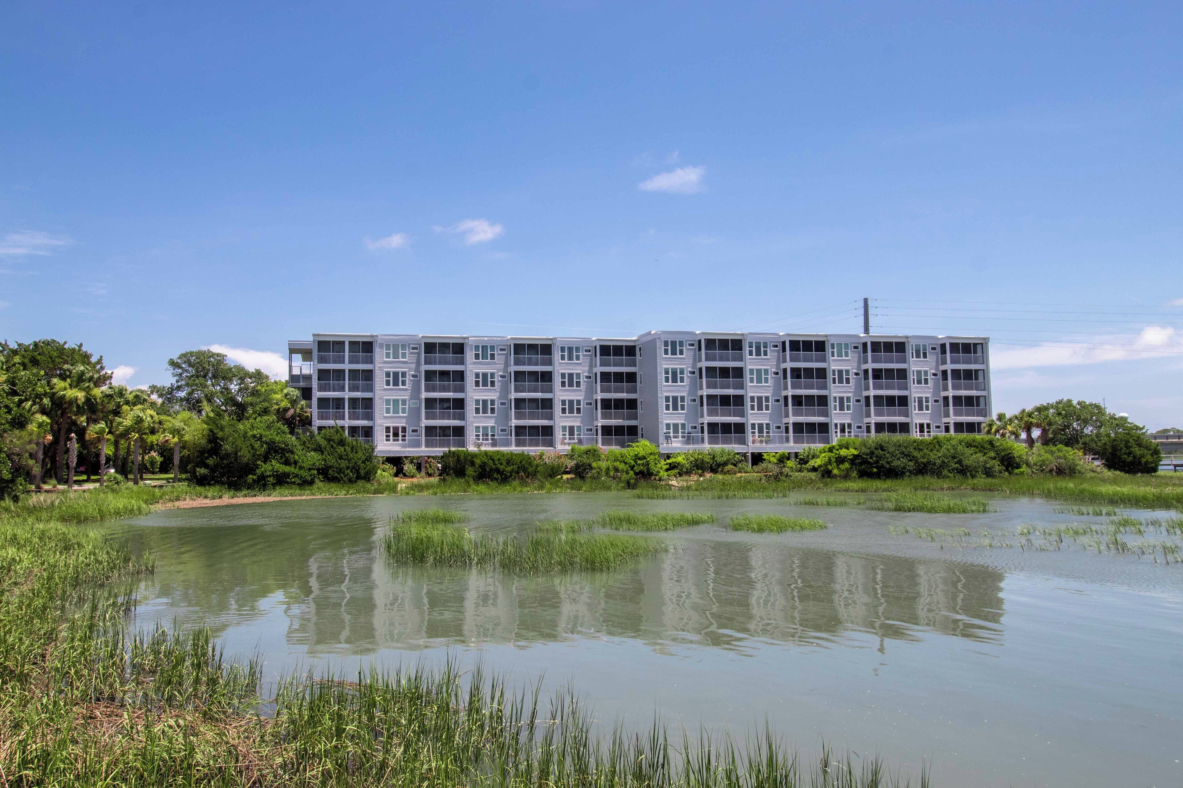 Un immeuble moderne à plusieurs étages, doté de balcons, entouré d’une étendue d’eau et de verdure.