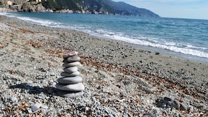 Una playa de guijarros con un montículo de piedras al frente y una vista costera con montañas en el fondo.