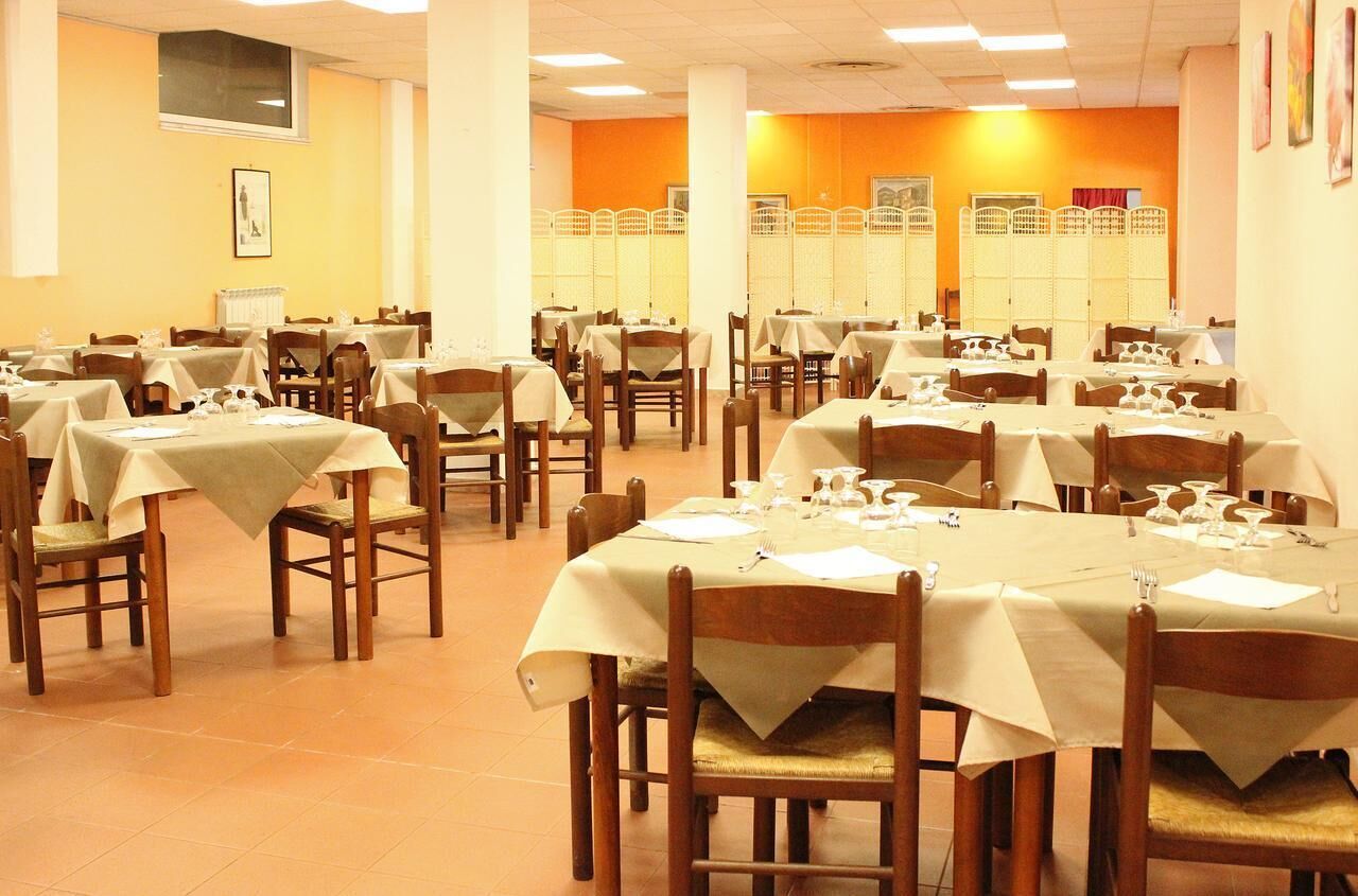 A dining area with multiple tables and chairs, each set with tablecloths and cutlery.
